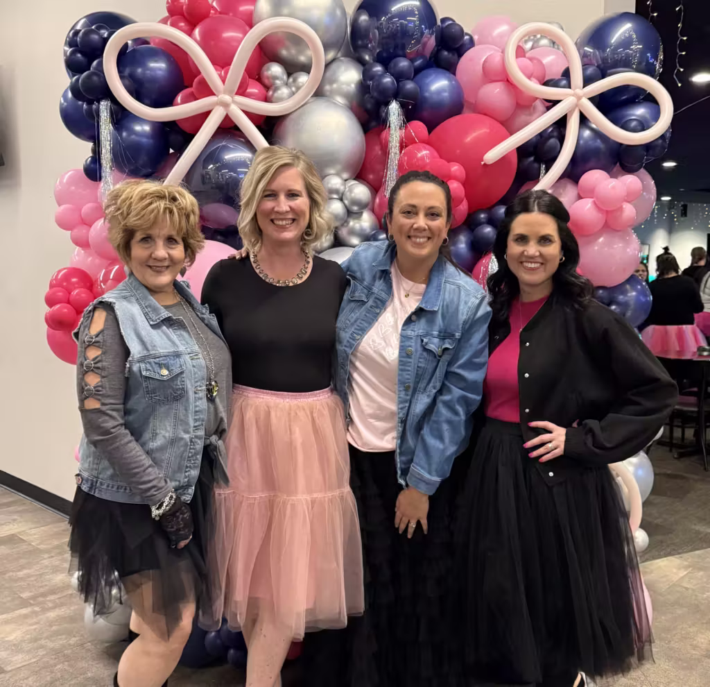 photo of Sharon, Sara Cipriano, Katie Barca, JoAnn Lewis posing for a photo in front of a balloon backdrop, all wearing tutus