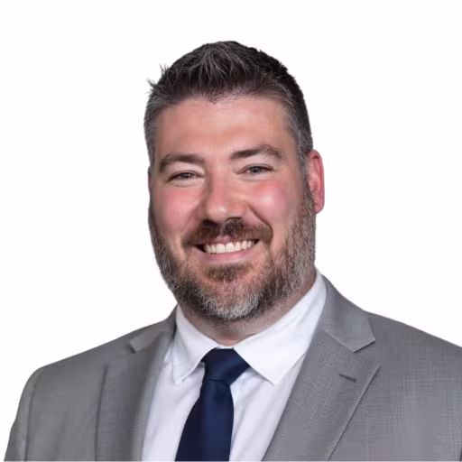 headshot for Austin Swift, wearing a grey suit and white shirt with a blue tie