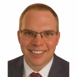 headshot of Ben Gaines wearing white shirt, red tie, and dark gray suit coat