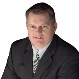 headshot of Billy Holloway, wearing a black suit with a striped tie