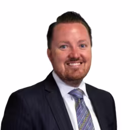 headshot of Charles Rogers, wearing a white shirt with a blue stripped tie and black suit jacket