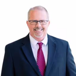 headshot of Chip Brother, wearing a black suit with a red tie