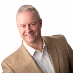 Headshot of Chuck Miller wearing white dress shirt and tan suit coat with white background