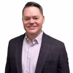 headshot of Dan Wenner, wearing a dark suit with a pink shirt
