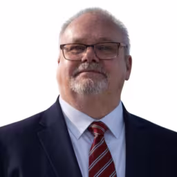 headshot of Dennis Marshall, wearing a black suit with a red tie