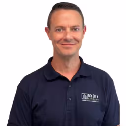 Headshot of Doug Searles wearing navy blue polo shirt with white background
