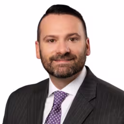 Headshot of Ed Charleson, wearing a black suit with a purple pinstripe tie.