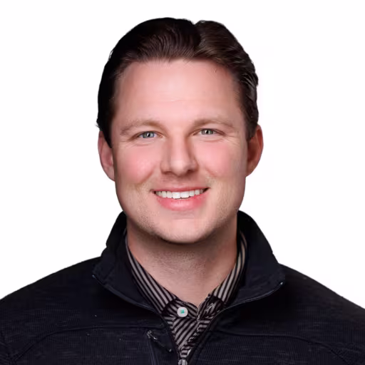 headshot of Elliot Blake, wearing a black sweater with a plaid shirt