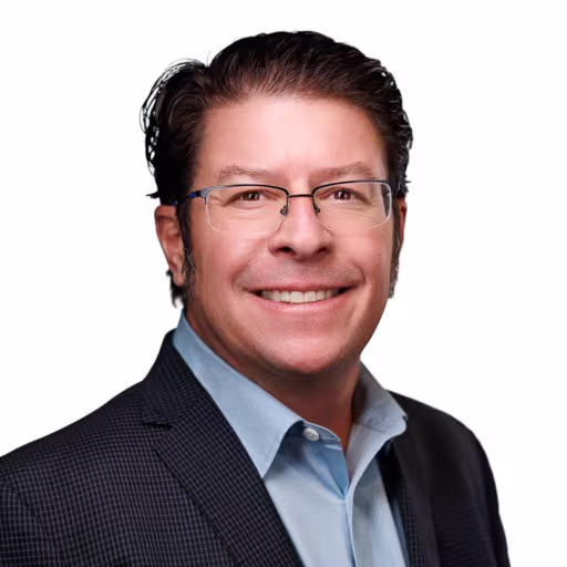 Headshot of Eric Pederson wearing light blue dress shirt and black checkered suit coat with white background