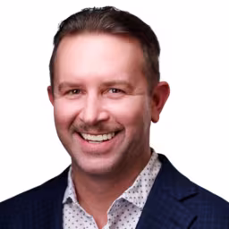 headshot of Jared Heesacker, wearing a dark blue suit with a polka dot shirt