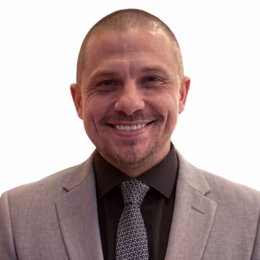 Headshot of Jimmy Litman wearing black dress shirt, black and grey tie, and grey suit coat with white background