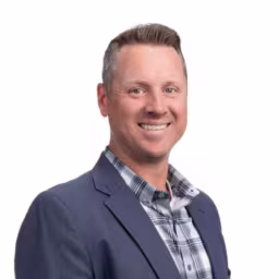 headshot of Jodi Ulrich, wearing a grey suit with a grey plaid shirt