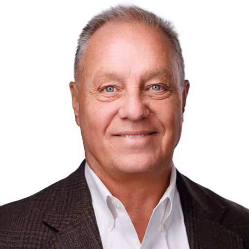 headshot of John McGinty, wearing a brown suit with a white shirt