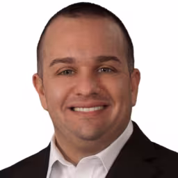 Headshot of Nick Rovella wearing white dress shirt and black suit coat with white background