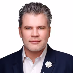headshot of Patrick Keelin, wearing a black suit with a white shirt