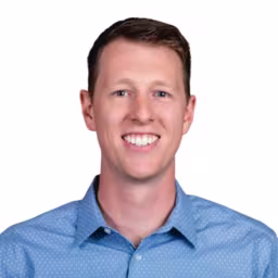 headshot of Taylor Heinrichs, wearing a light blue button up