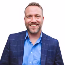 headshot of Travis Nicolaysen, wearing a blue suit and shirt
