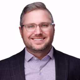 Headshot of Zack Disinger wearing purple dress shirt and dark grey checkered suit coat with white background