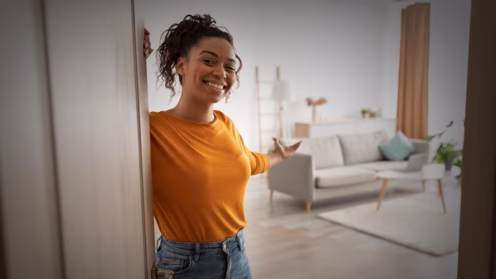 Cheerful African Woman Opening Door Welcoming You Standing At Home