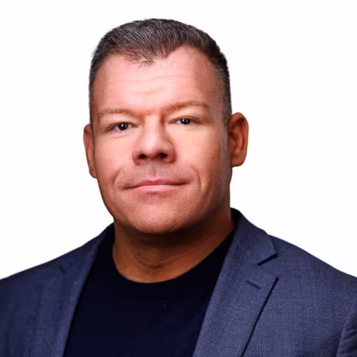 headshot of James Thom, wearing a blue suit with a black shirt