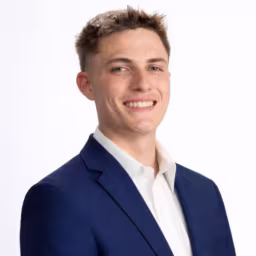 headshot of Brody Quillin in white button up shirt and dark navy suit jacket with white background