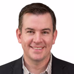 headshot of Mark Kidd, wearing a black suit and striped shirt