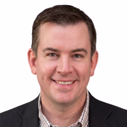 headshot of Mark Kidd, wearing a black suit and striped shirt
