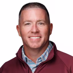 headshot of Markus Spicer, wearing a red pull over with a stripped shirt