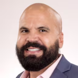 headshot of AJ Alvarez wearing a dark grey suit and pink shirt