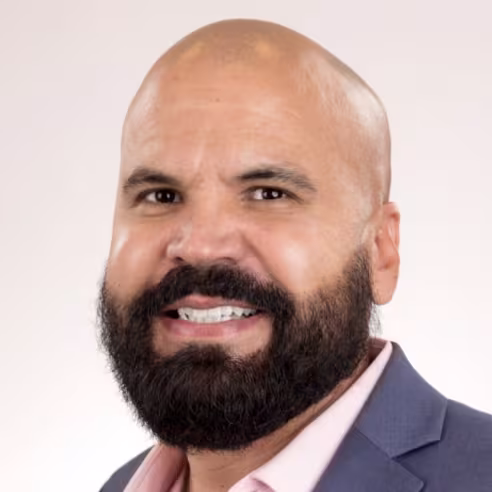 headshot of AJ Alvarez wearing a dark grey suit and pink shirt