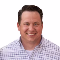 Headshot of Bill Barnes wearing white and dark blue checkered dress shirt with white background
