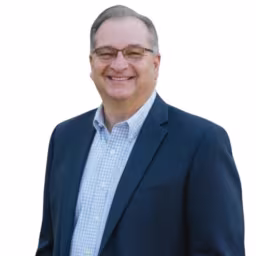 Headshot of John Kane wearing light blue and white checkered dress shirt and dark blue suit coat with white background