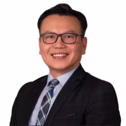 headshot of Steven Vo, wearing a black suit with a light blue shirt and blue and white stripped tie